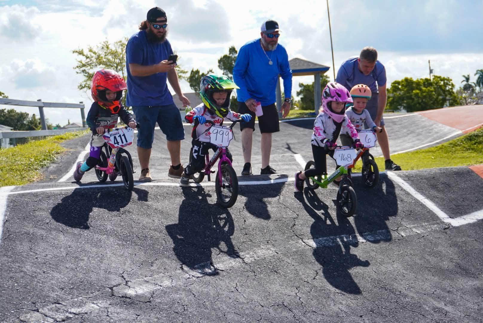 Four balance bike racers on the starting gate with their parents behind them