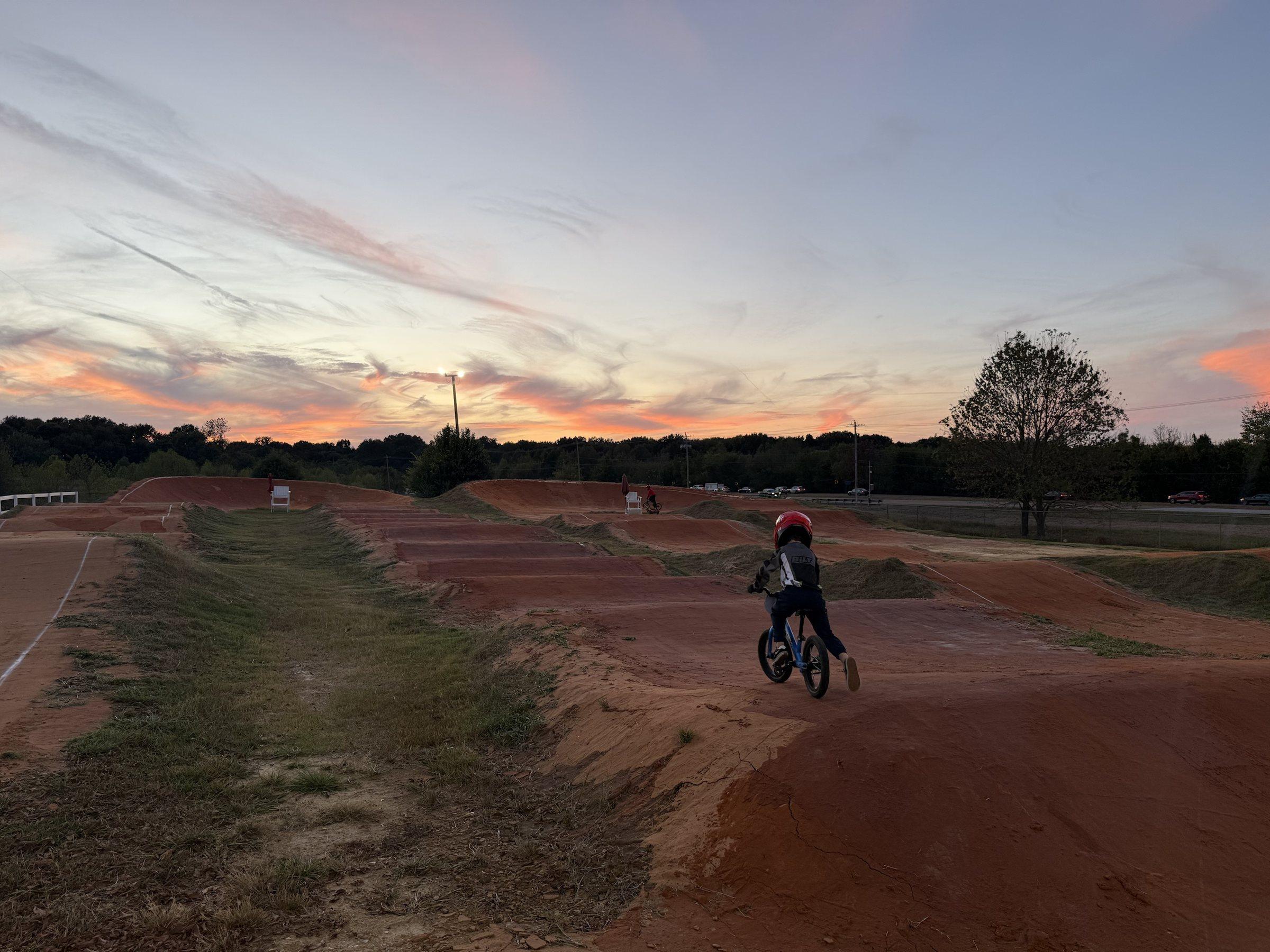 A young rider on a balance bike rolling through the rhythm section at sunset