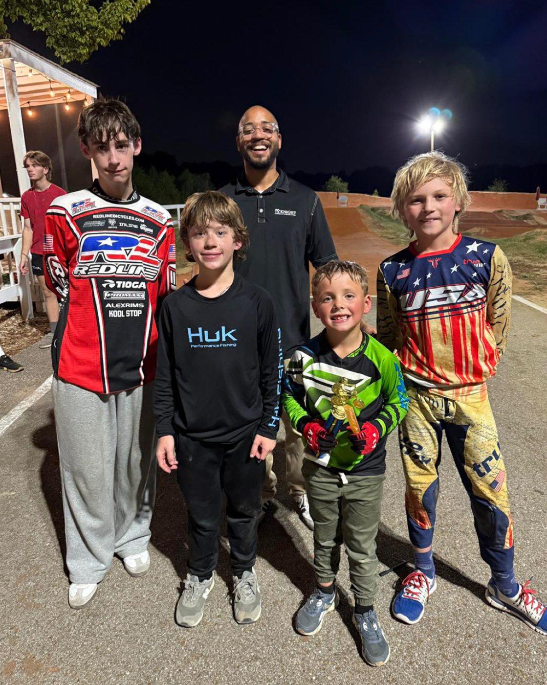 Four young riders and a coach standing together at the track under the lights