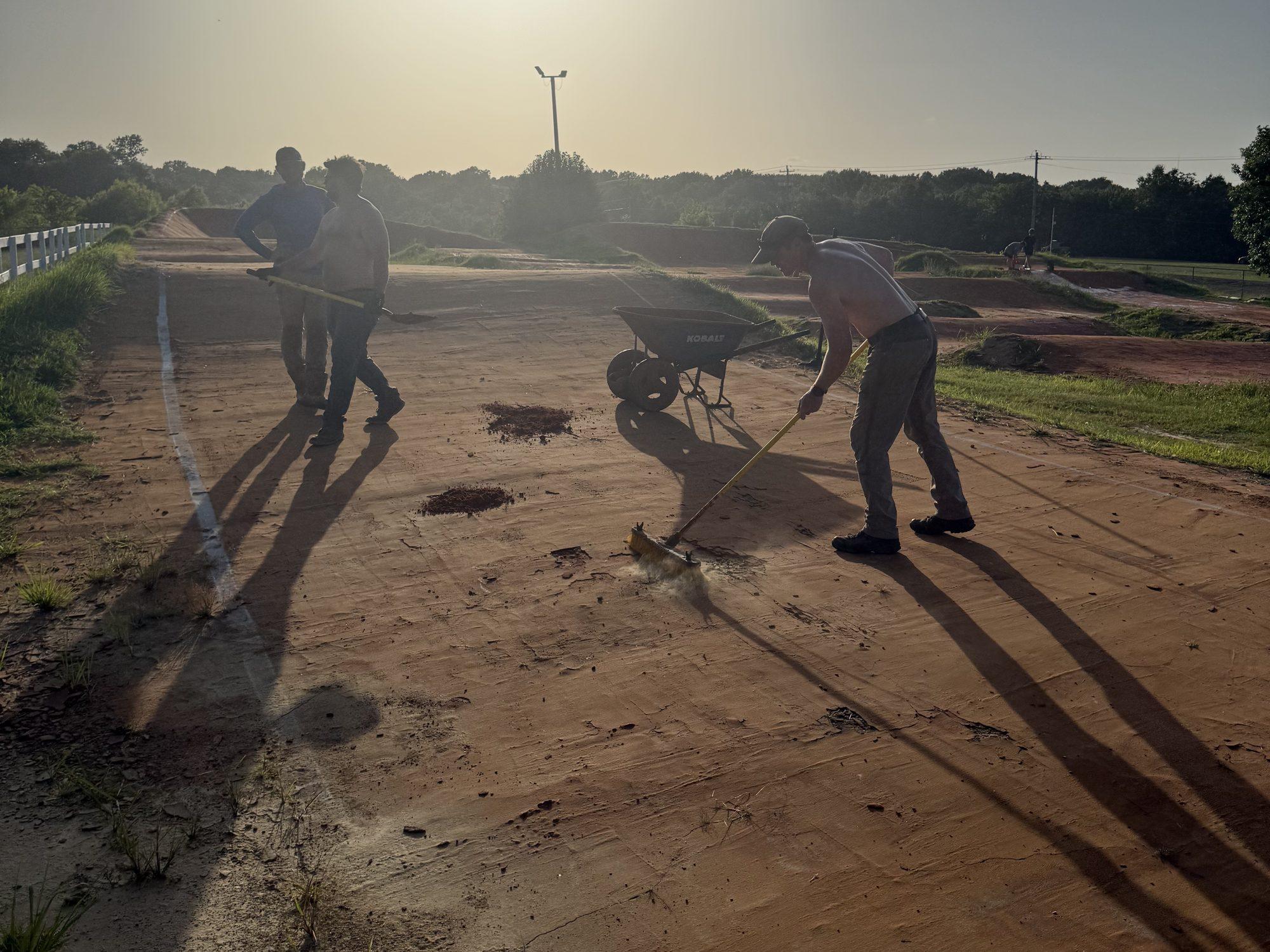 Volunteers raking and sweeping the track surface at sunset